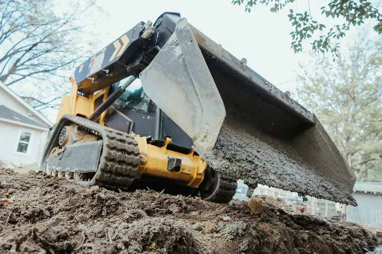Skid-steer bucket lifting subsoil out of a back-yard trench
